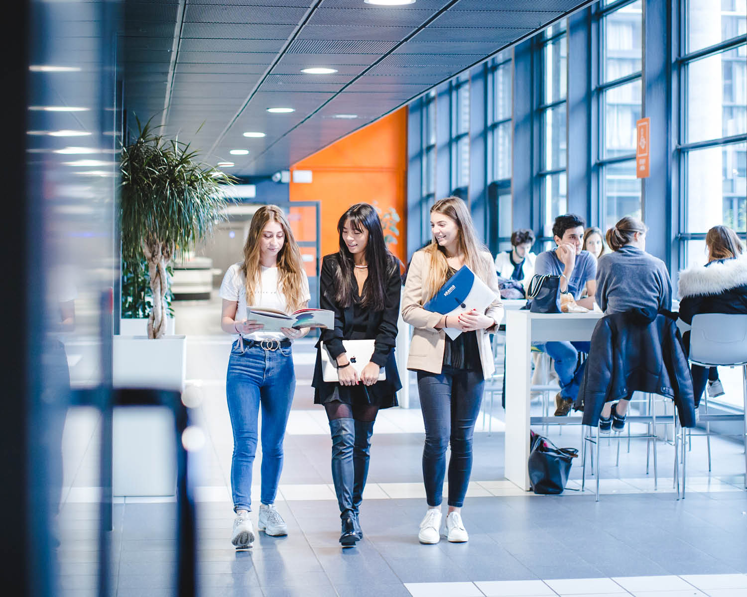 3 étudiantes marchent dans l'école en se montrant des brochures